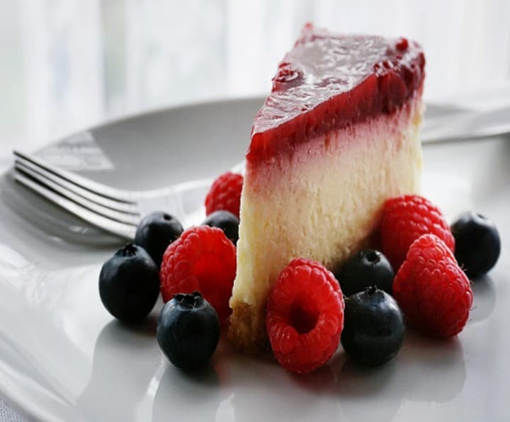 Slice of cheesecake with berry glaze and fresh raspberries and blueberries
